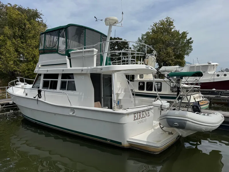 Slide: The Image of 2001 Mainship 390 yacht docked, featuring green canopy and inflatable dinghy, surrounded by other boats. - 2