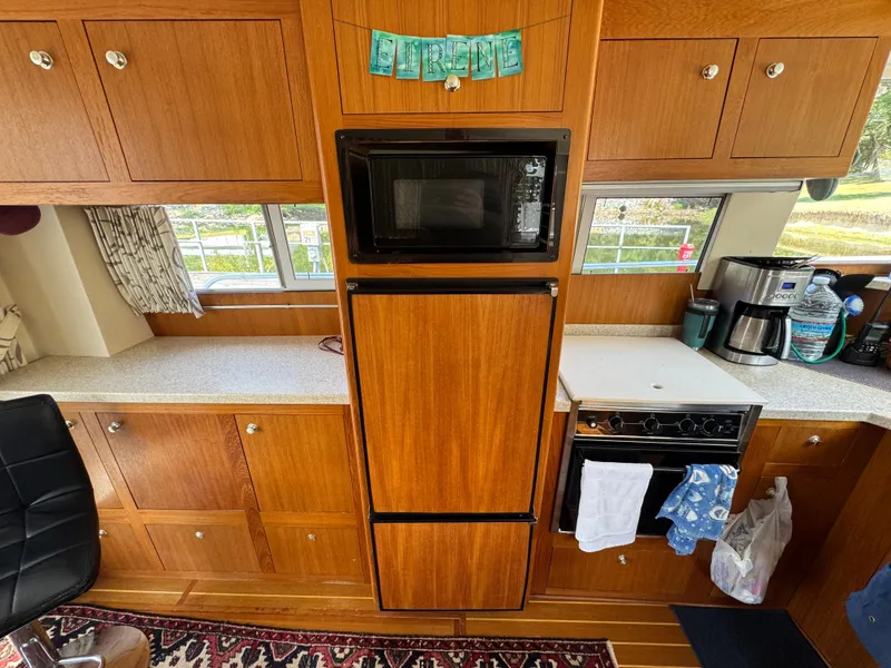Slide: The Image of 2001 Mainship 390 kitchen with wooden cabinets, microwave, and stove, featuring a cozy interior design. - 41