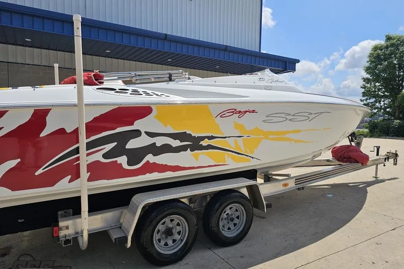 Slide: The Image of 2002 Baja 25 Outlaw boat with vibrant graphics on a trailer, parked outdoors. - 10