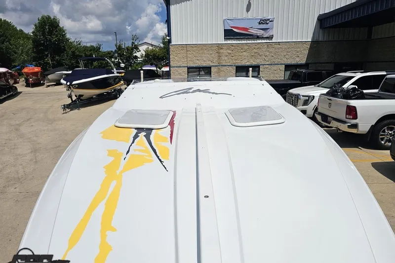 Slide: The Image of 2002 Baja 25 Outlaw boat with vibrant graphics, parked outdoors near other vehicles. - 17