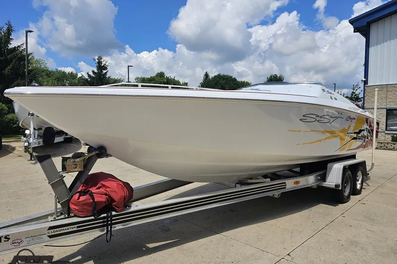 Slide: The Image of 2002 Baja 25 Outlaw boat on trailer, parked outdoors under a cloudy sky. - 18