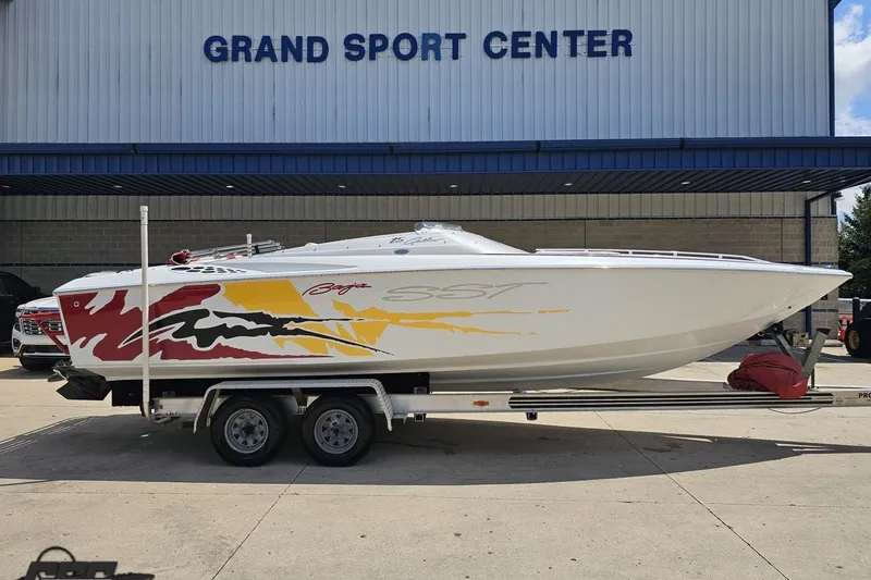 Slide: The Image of 2002 Baja 25 Outlaw boat with colorful graphics on a trailer at Grand Sport Center. - 2