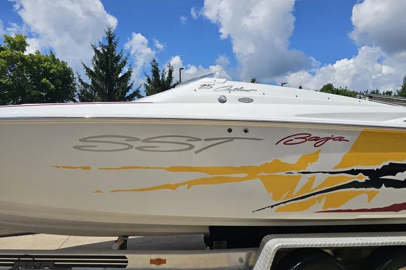 Slide: The Image of 2002 Baja 25 Outlaw boat with vibrant graphics, parked on a trailer under a blue sky. - 21