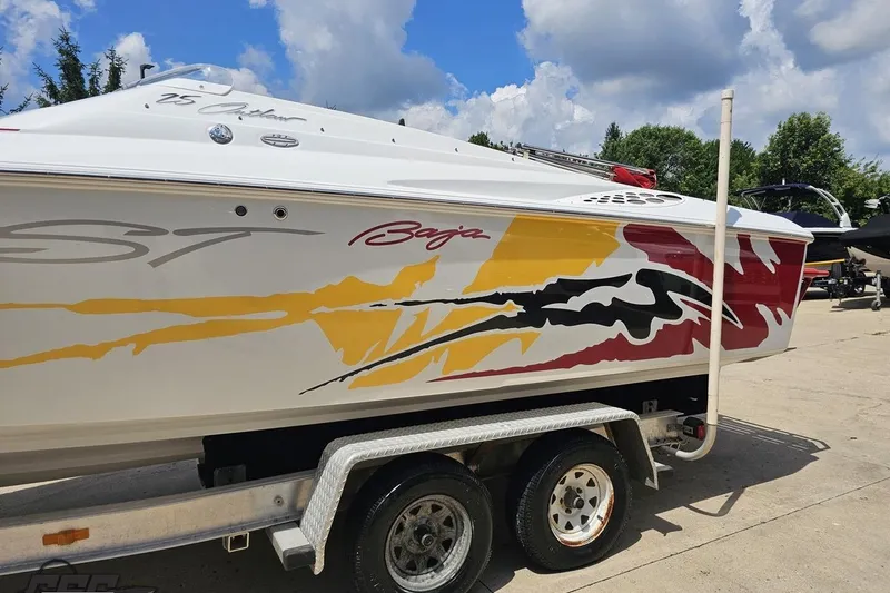 Slide: The Image of 2002 Baja 25 Outlaw boat with vibrant graphics on a trailer under a blue sky. - 23