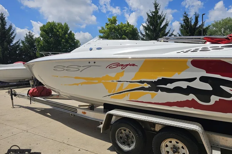 Slide: The Image of 2002 Baja 25 Outlaw boat with vibrant graphics on a trailer, under a clear blue sky. - 26