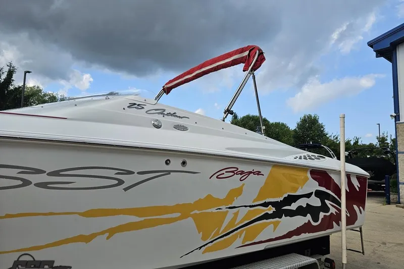 Slide: The Image of 2002 Baja 25 Outlaw boat with vibrant graphics, parked under a cloudy sky. - 43