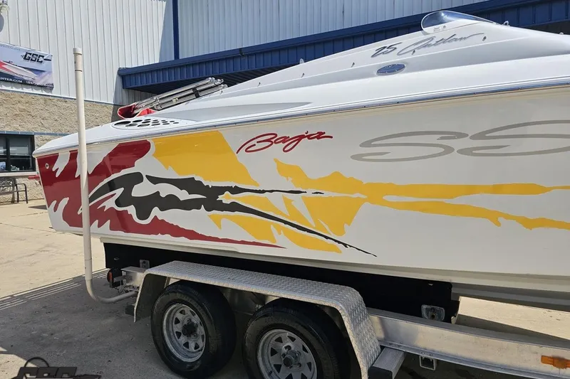 Slide: The Image of 2002 Baja 25 Outlaw boat with vibrant red, yellow, and black graphics on a trailer. - 6