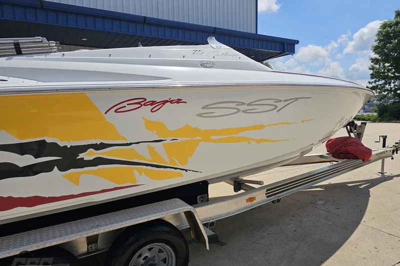 Slide: The Image of 2002 Baja 25 Outlaw boat with vibrant graphics on a trailer, parked outdoors. - 9