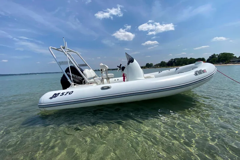 Slide: The Image of 2013 Mercury Inflatables M570 boat floating on clear water under a blue sky. - 0