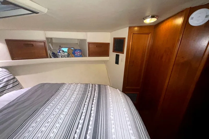 Slide: The Image of 1996 Riviera 39 Open Flybridge cabin interior with bed, wooden cabinets, and striped bedding. - 24