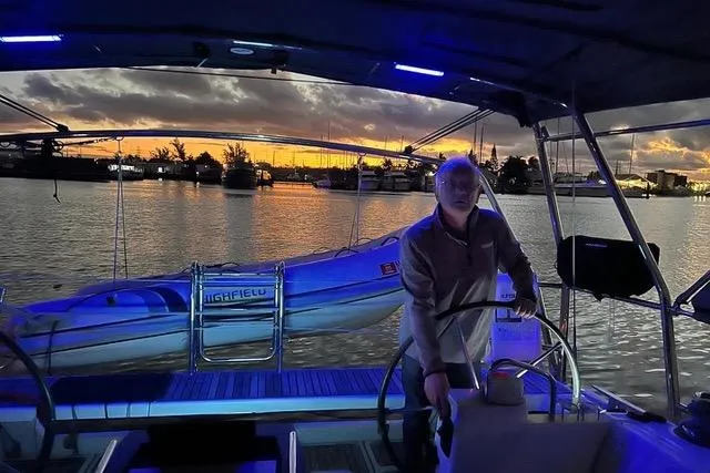 Slide: The Image of Man steering 2013 Beneteau Oceanis 45 sailboat at sunset, with vibrant sky and calm waters. - 43