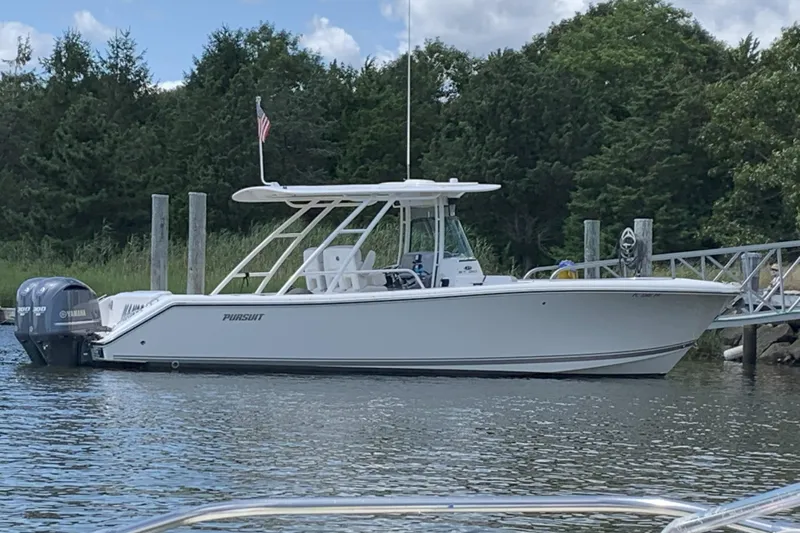 Slide: The Image of 2014 Pursuit ST 310 Sport boat docked by a lush, green shoreline. - 1