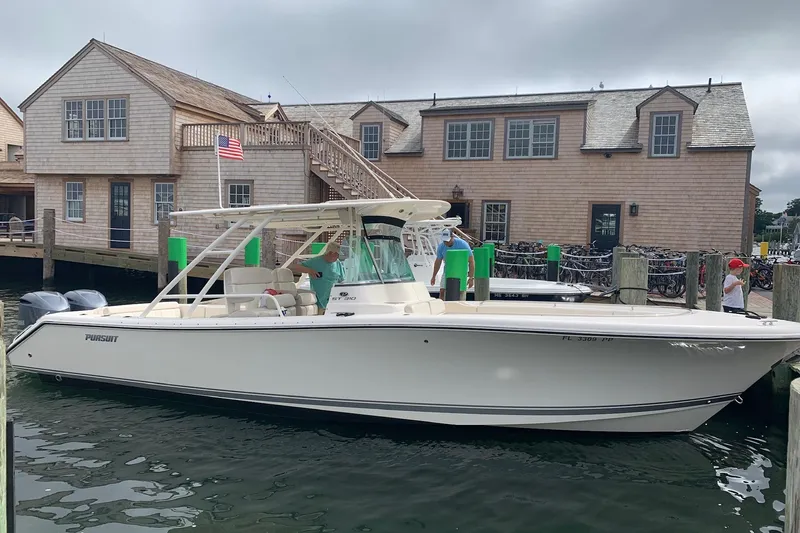 Slide: The Image of 2014 Pursuit ST 310 Sport boat docked near wooden building with American flag. - 2