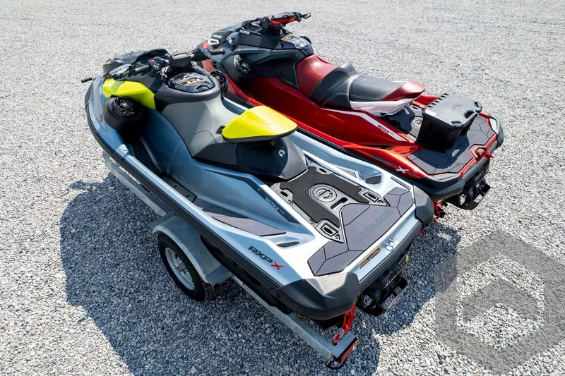 Slide: The Image of 2024 Sea-Doo RXP-X 325 jet skis on a trailer, parked on gravel. - 50