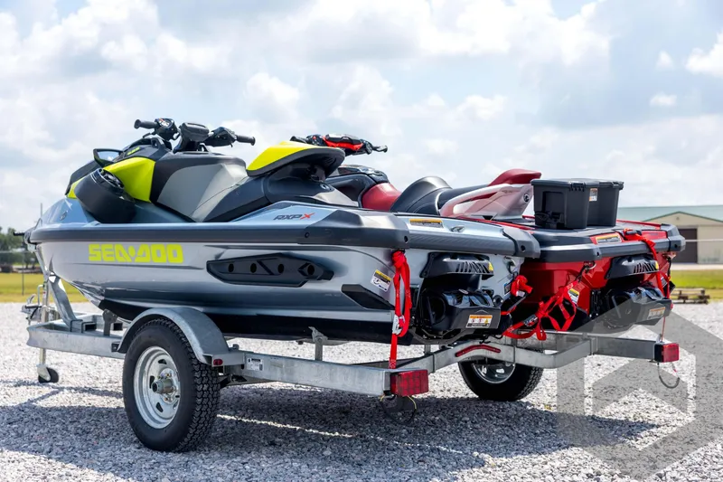 Slide: The Image of 2024 Sea-Doo RXP-X 325 jet skis on trailer, parked on gravel under blue sky. - 7