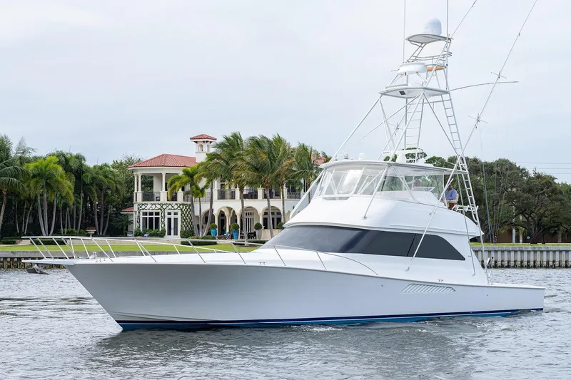 Slide: The Image of 2005 Viking 61 yacht cruising near a luxurious waterfront mansion with palm trees. - 99