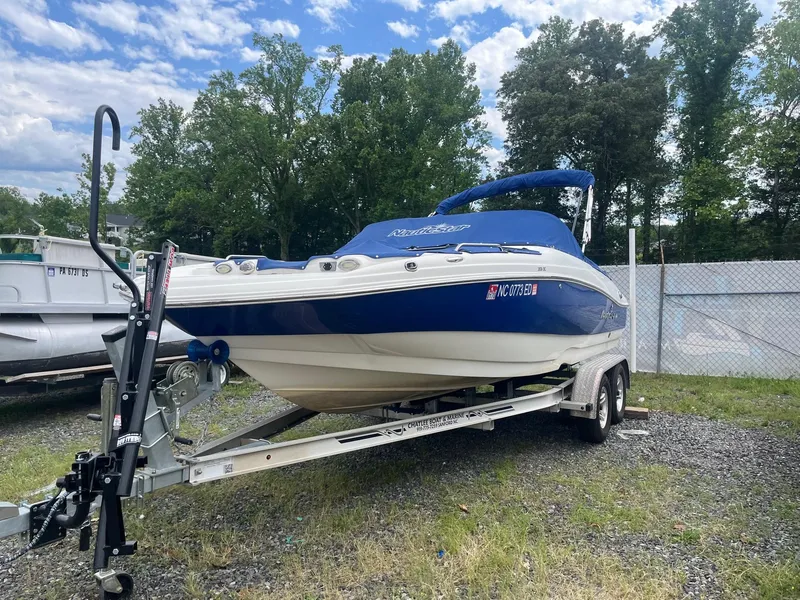 The Image of 2016 NauticStar 203DC Sport Deck boat on trailer, blue cover, parked outdoors. - 0