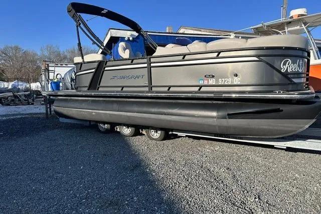 Slide: The Image of 2021 Starcraft SLS 1 pontoon boat on trailer, parked on gravel lot. - 5