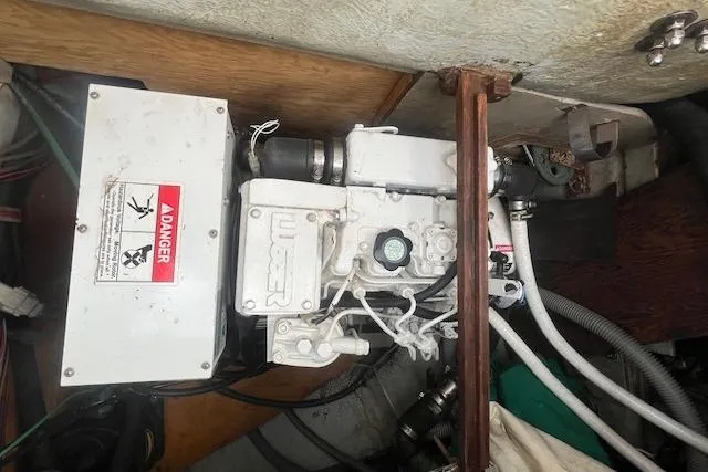 Slide: The Image of Engine compartment of a 1983 Baba 40 sailboat, featuring mechanical components and warning label. - 27