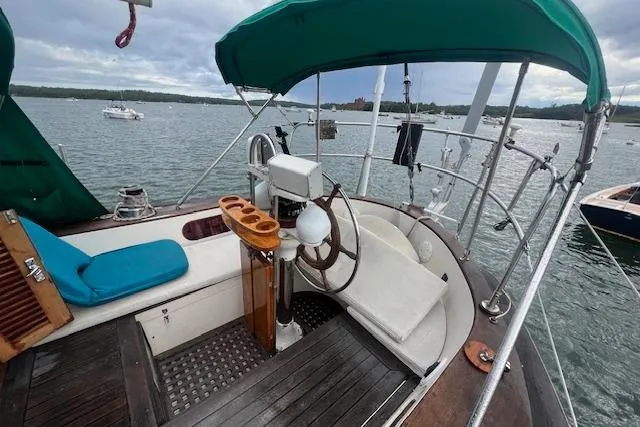 Slide: The Image of Cockpit of 1983 Baba 40 sailboat with green canopy and wooden accents on a calm lake. - 35