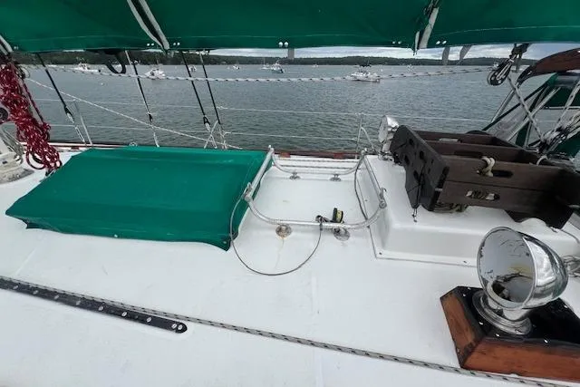 Slide: The Image of 1983 Baba 40 sailboat deck with green cover, moored in a scenic harbor. - 37