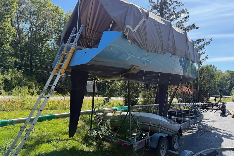 Slide: The Image of 2007 Hallett 33 boat on trailer with cover, ladder, and greenery background. - 2