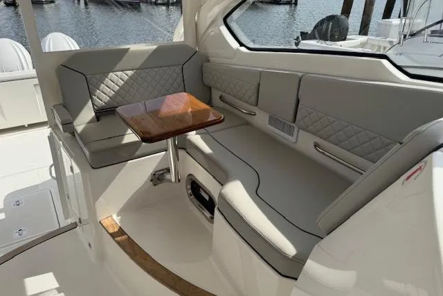 Slide: The Image of 2025 Pursuit DC 365 Dual Console boat interior with cushioned seating and wooden table. - 19