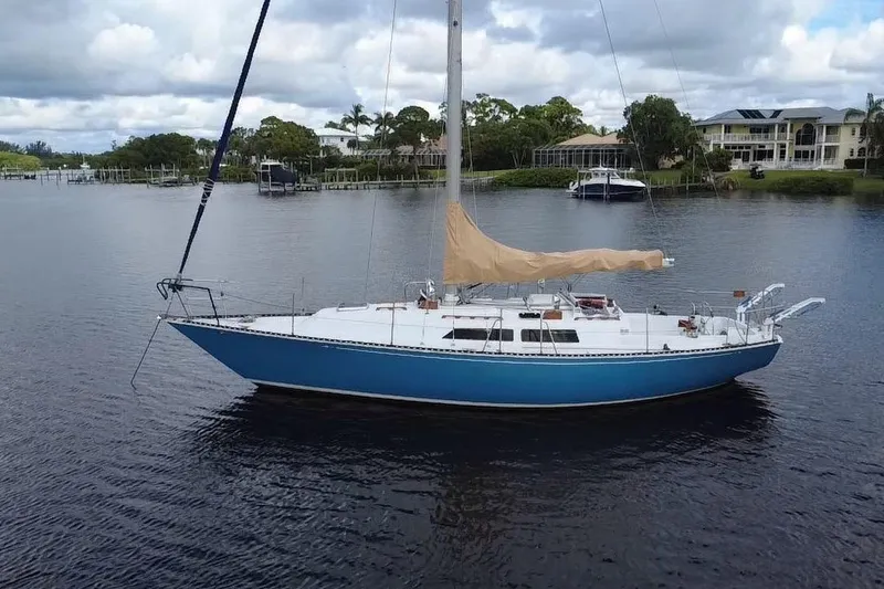 Slide: The Image of 1980 C&C Landfall 38 sailboat on calm water, surrounded by lush greenery and houses. - 22