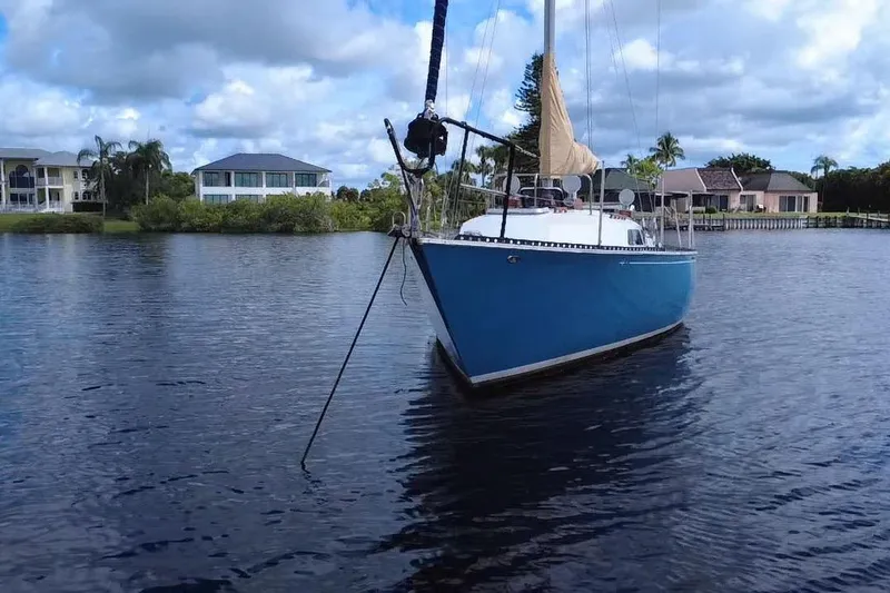 Slide: The Image of 1980 C&C Landfall 38 sailboat anchored on a calm waterway with houses in the background. - 48