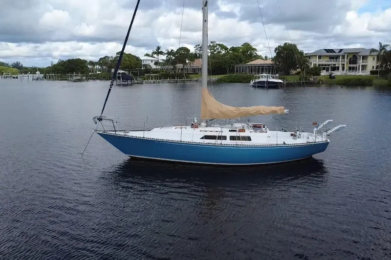 Slide: The Image of 1980 C&C Landfall 38 sailboat with blue hull on calm water, surrounded by lush greenery. - 56