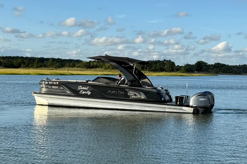 Slide: The Image of 2025 Avalon Excalibur Quad Lounge Windshield boat cruising on a serene lake. - 4