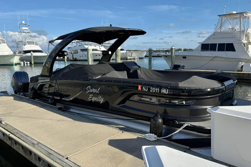 Slide: The Image of 2025 Avalon Excalibur Quad Lounge Windshield boat docked at marina, covered and sleek. - 45