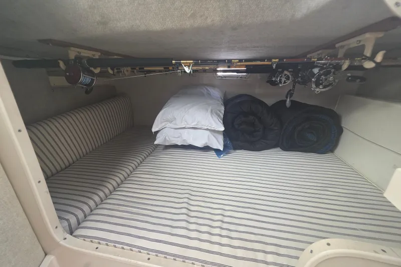 Slide: The Image of 1990 Grady-White Marlin 280 cabin interior with striped bedding and fishing rods. - 25