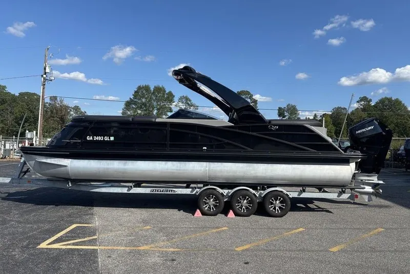 Slide: The Image of 2024 Bennington 25 QFBWA pontoon boat on trailer, parked outdoors under blue sky. - 2