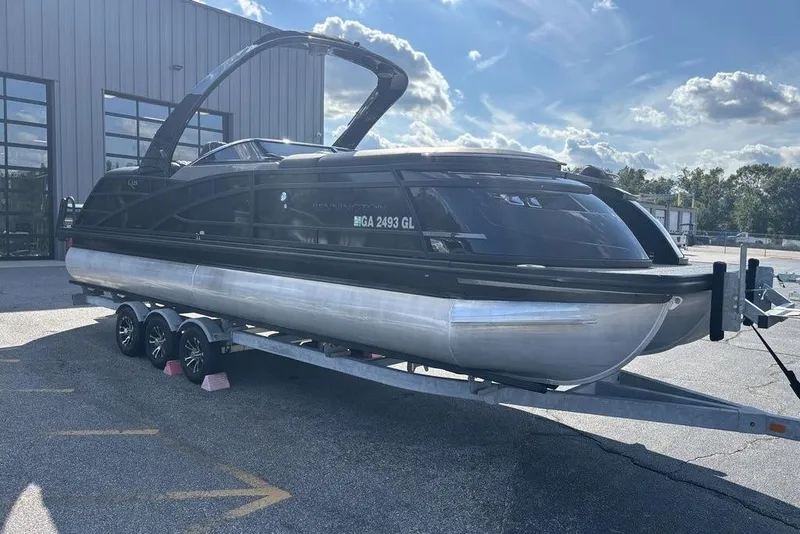 Slide: The Image of 2024 Bennington 25 QFBWA pontoon boat on trailer, parked outdoors under a blue sky. - 3