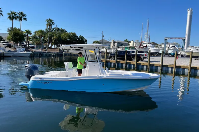 Slide: The Image of 2026 Caymas 24 HB boat in marina, surrounded by palm trees and clear blue water. - 2