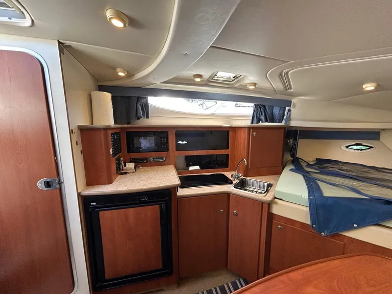 Slide: The Image of 2007 Bayliner 305 interior with kitchenette, sink, and bed. Cozy and well-lit cabin space. - 23