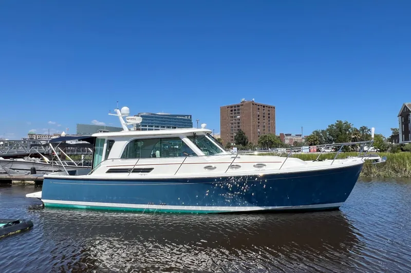 Slide: The Image of 2016 Back Cove 37 boat docked on a sunny day, with cityscape background. - 1