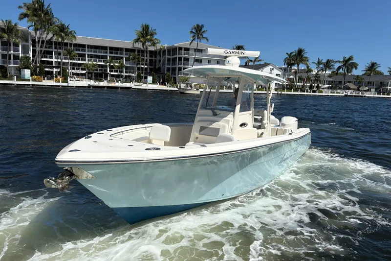 Slide: The Image of 2018 Cobia 301 Center Console boat cruising on water near waterfront buildings. - 12