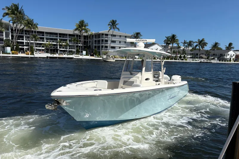 Slide: The Image of 2018 Cobia 301 Center Console boat cruising on a sunny waterfront with palm trees. - 13