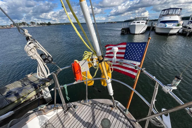 Slide: The Image of 1982 Tayana 37 sailboat docked, featuring American flag and nautical equipment, under a partly cloudy sky. - 19