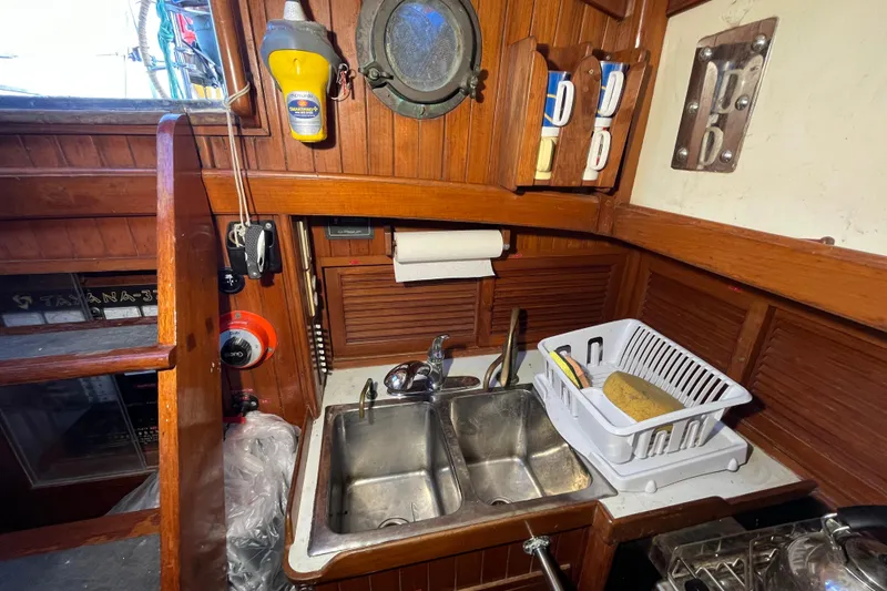 Slide: The Image of 1982 Tayana 37 yacht kitchen with wooden cabinetry, dual sink, and dish rack. - 27