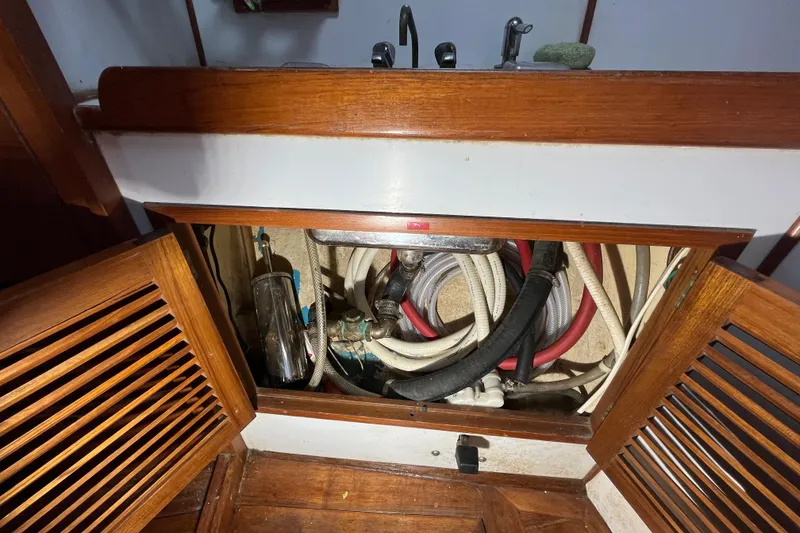 Slide: The Image of 1982 Tayana 37 sailboat plumbing system with exposed pipes and wooden cabinetry. - 62