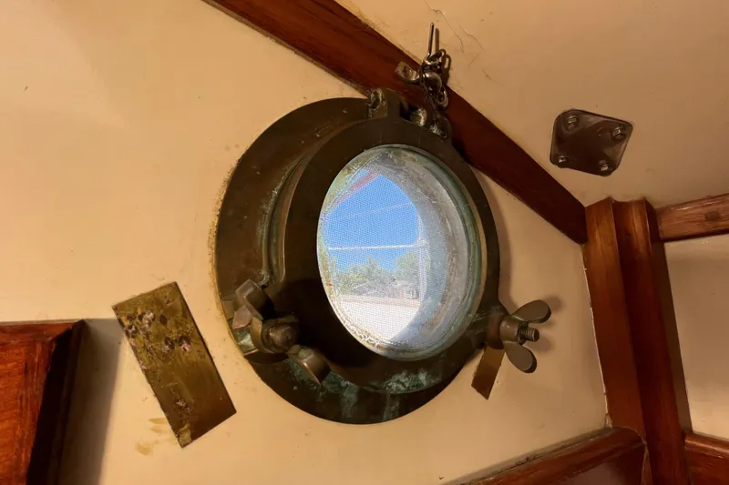 Slide: The Image of Circular porthole on 1982 Tayana 37 sailboat, featuring brass fittings and wooden trim. - 67