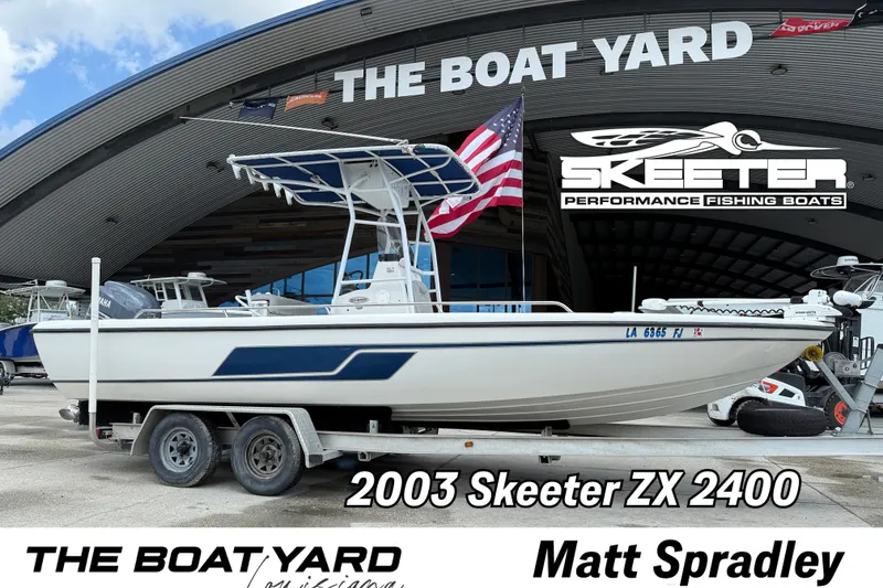 Slide: The Image of 2003 Skeeter ZX2400 boat on trailer with American flag, parked outside a building. - 1