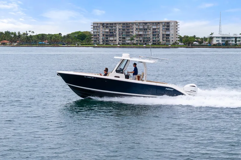 Slide: The Image of 2019 Pursuit S 288 Sport boat cruising on open water with city skyline backdrop. - 9