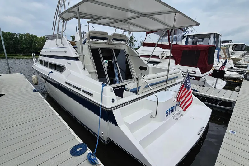 Slide: The Image of 1990 Carver 3467 Santego yacht docked, featuring spacious deck and American flag. - 2