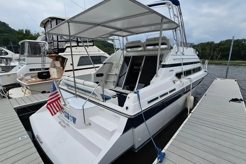 Slide: The Image of 1990 Carver 3467 Santego yacht docked, featuring spacious deck and American flag. - 3