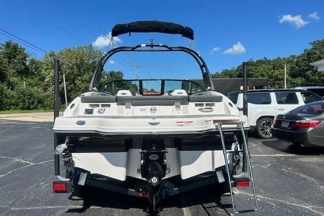 Slide: The Image of 2026 Chaparral 21 SSi boat, rear view, parked on asphalt under clear blue sky. - 2