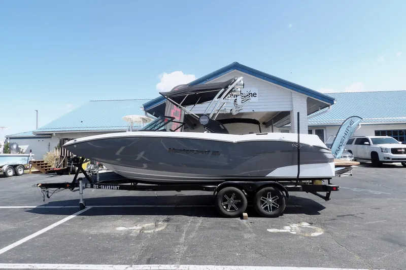 The Image of 2023 MasterCraft NXT22 boat on trailer, parked outside a building under clear sky. - 1